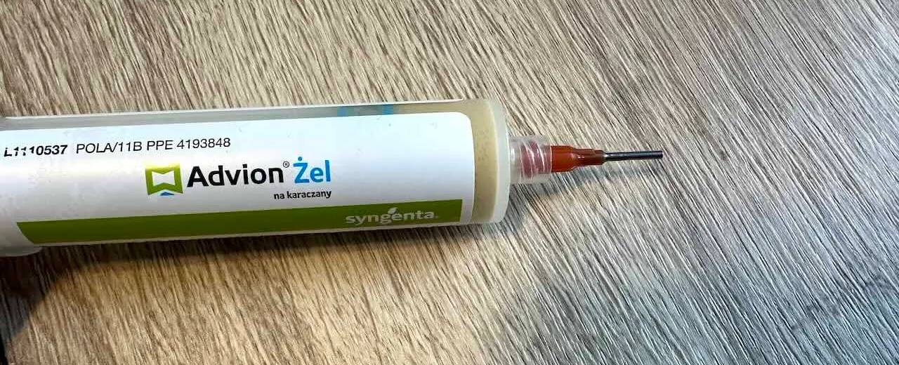 Strzykawka Advion Żel z nałożoną pomarańczową igłą dozowniczą, leżąca na podłodze z paneli