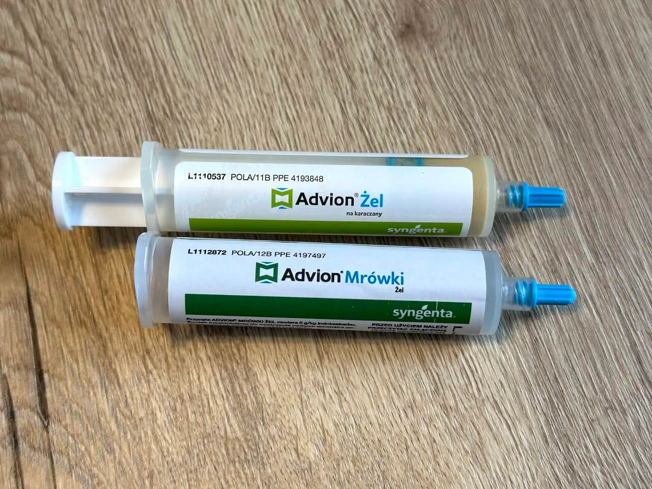 Dwie strzykawki Syngenta leżące na podłodze: Advion Żel na karaczany i Advion Mrówki Żel, obie z niebieskimi zatyczkami